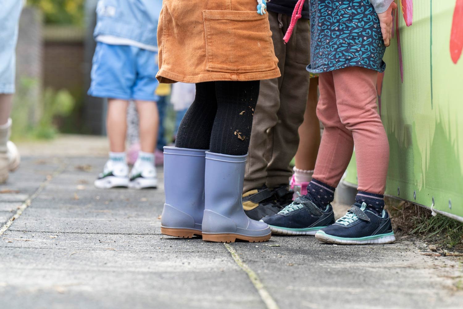 Children wearing boots and colorful clothes outdoors.