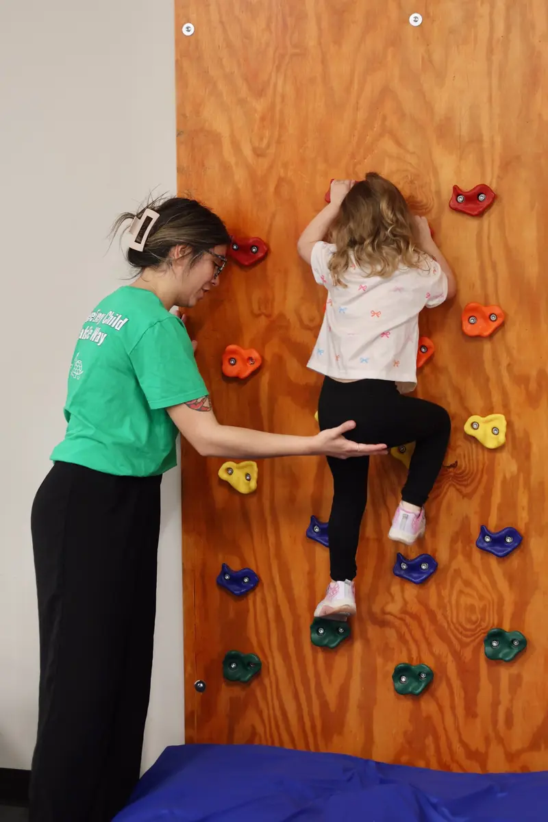 Child climbing an indoor activity wall with support from an AB Spectrum team member